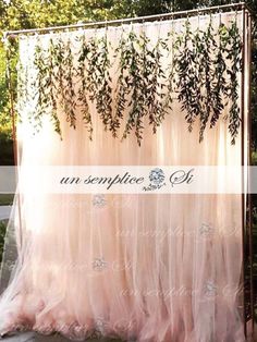 an outdoor wedding ceremony with pink tulle and greenery hanging from the back wall