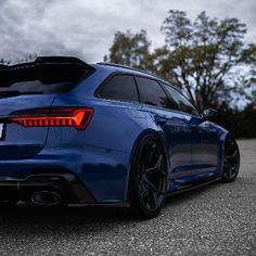 the rear end of a blue car parked in a parking lot with cloudy skies behind it