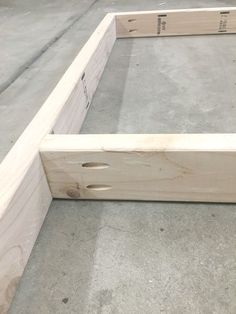 an unfinished bed frame sitting on top of cement floor next to a wooden box with holes in it