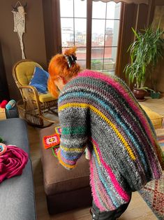 a woman in a brightly colored sweater is looking out the window at her living room