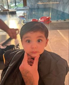 a young boy sitting in a chair with his hand on his chin and looking at the camera