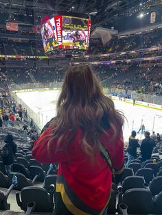 a woman sitting in front of an ice hockey rink with her back to the camera