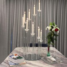 there are many candles on the table with flowers in vases next to each other