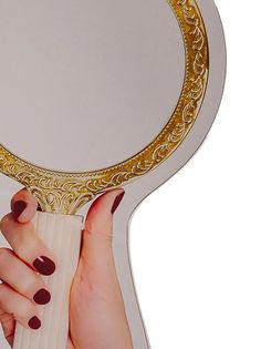 a woman's hand holding up a mirror with gold trimmings on it