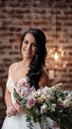 a woman holding a bouquet of flowers in front of a brick wall with lights on it