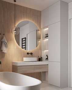 a white bath tub sitting next to a bathroom sink under a round mirror on the wall