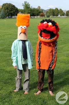 two people dressed as sesame and the muppet are standing on grass in front of a park