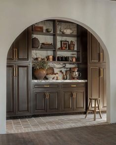 an arched doorway leads into a kitchen with marble counter tops and wooden cabinets, along with brass accents