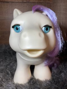 a white pony with purple hair and blue eyes sitting on top of a gray rug