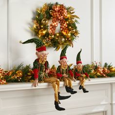 two elf figurines sitting on top of a mantle next to a christmas wreath