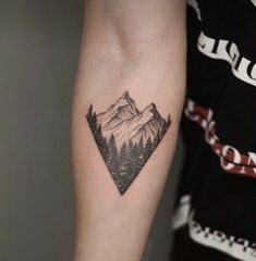 a man's arm with a mountain and pine tree tattoo on the left forearm