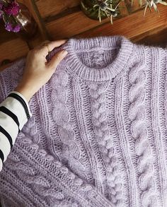 a woman's hand on top of a purple knitted sweater next to potted plants