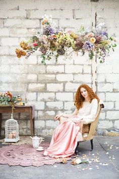 a woman sitting in a chair with flowers hanging from the ceiling