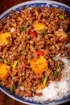 a blue and white bowl filled with rice and meat on top of a wooden table