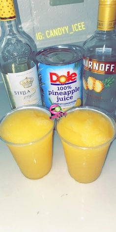 two glasses filled with orange juice next to bottles of vodka and pineapple juice on a counter