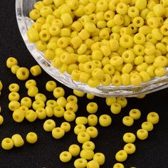 yellow seed beads in a bowl on a black surface with other beads scattered around it