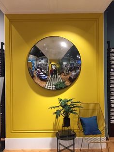 a yellow wall with a round mirror hanging on it's side next to a chair and potted plant