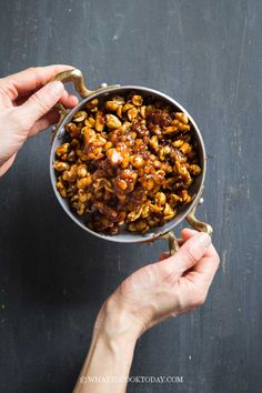 two hands holding a metal bowl filled with nuts