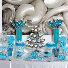 a table topped with blue and white cupcakes next to an art work on the wall