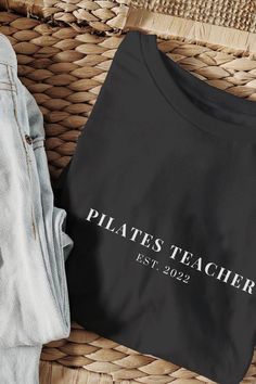 a black t - shirt that says pilates teacher on it next to some jeans