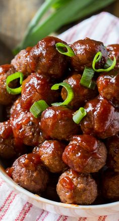 a bowl filled with meatballs covered in sauce and green onions on top of a table