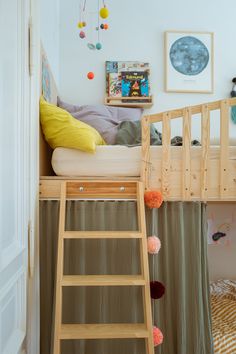 a small child's bed with a ladder to the bottom and a wall hanging above it