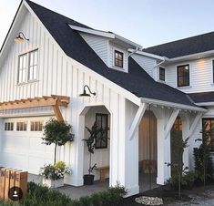 a white house with black shingles and windows on the front door is surrounded by greenery