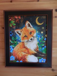 a cross stitch picture of a red fox sitting in the grass with a moon behind it