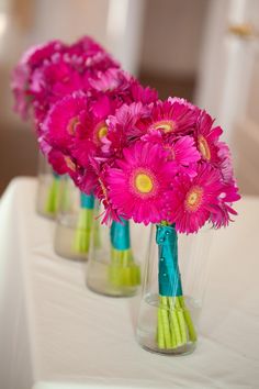 pink flowers in vases sitting on a table with green stems and blue ribbon around them