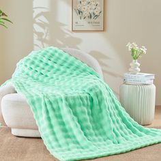 a green blanket sitting on top of a white couch next to a vase with flowers