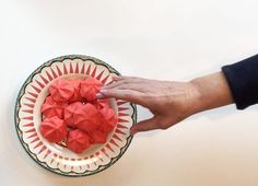 a person holding a plate with red food on it and another hand reaching for something