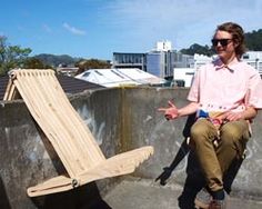 a man sitting on top of a roof next to a wooden chair with one leg up