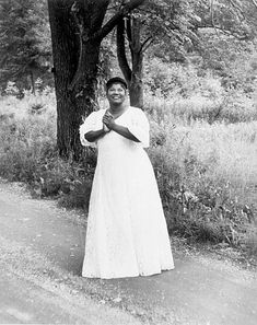 an old photo of a woman standing in front of a tree with her hands together