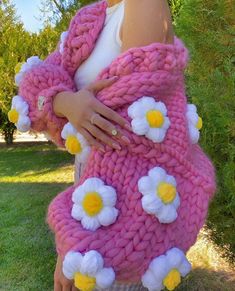 a woman wearing a pink sweater with white flowers on it and holding onto her arms