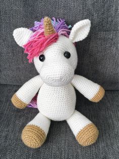 a crocheted unicorn stuffed animal with pink hair on it's head sitting on a couch