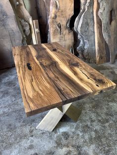 a wooden table sitting on top of a floor next to some rocks and wood logs