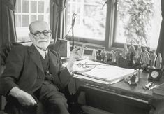 an old man sitting at a desk in front of a window with toy airplanes on it