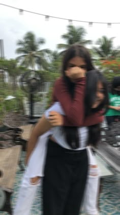 two people hugging each other in the middle of a courtyard with palm trees behind them