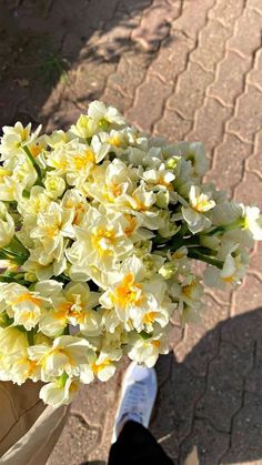 a person holding a bouquet of white and yellow flowers in their hand on the sidewalk