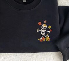 a black shirt with a skeleton and autumn leaves on the front is laying on a white surface