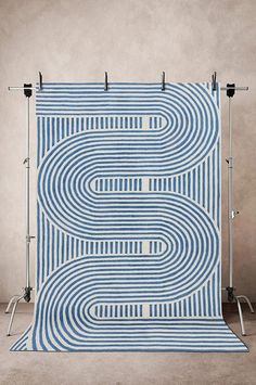 a blue and white rug with lines on it in front of a gray wall,