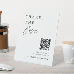 a white sign sitting on top of a wooden table next to a cup of coffee