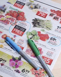 two pens sitting on top of a magazine next to some fruit and vegetables for sale