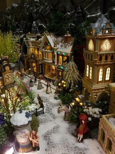 a christmas village is shown with lights and ornaments on the ground, including trees, buildings, and people