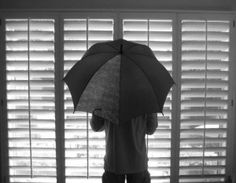 a person standing in front of a window with an umbrella over their head, looking out the window