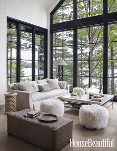 a living room filled with lots of windows next to a white couch and ottomans