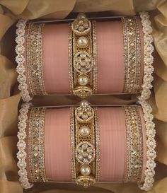 two pink and gold bracelets in a box with some pearls on it's sides