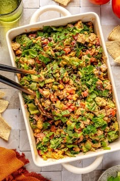 a white casserole dish filled with salad and tortilla chips on the side