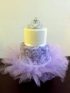 a three tiered cake with purple tulle and yellow top sitting on a table