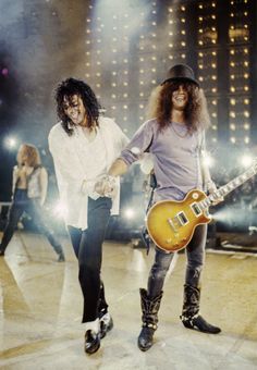 two people on stage with guitars and one person in the background holding an electric guitar